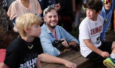 Doug Breault holds a camera as he is surrounded by young campers.